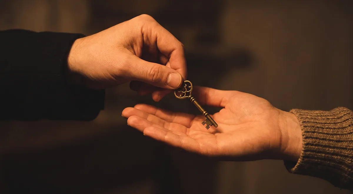 Two adults' hands passing a single key, a quiet gesture of trust and consent